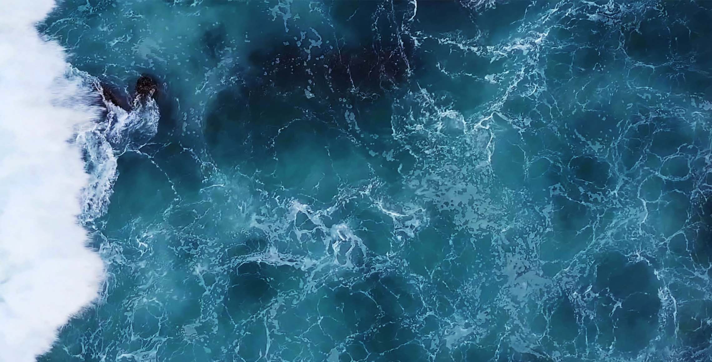 Aerial view of ocean waves crashing, creating white foam on blue water.