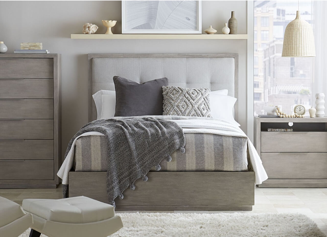 A cozy bedroom featuring a gray bed, a dresser, and a nightstand, creating a serene and stylish atmosphere.