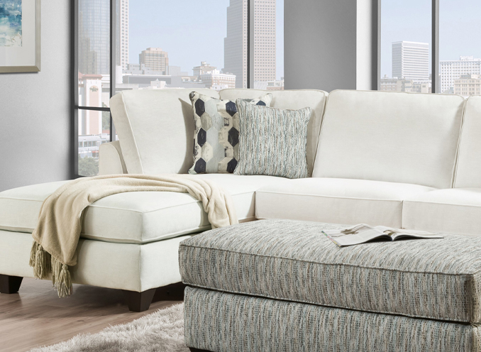 A white sectional couch adorned with decorative pillows and accompanied by a matching ottoman, creating a cozy living space.