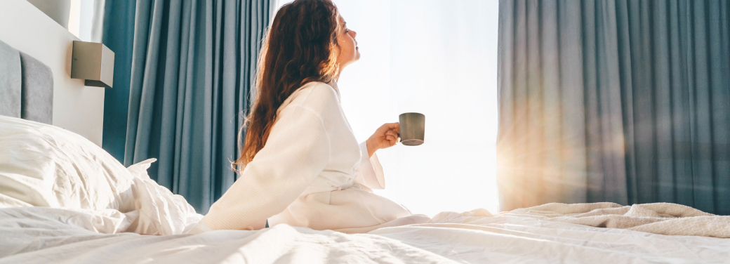 Woman sitting up in bed under the sunlight enjoying a hot cup of coffee