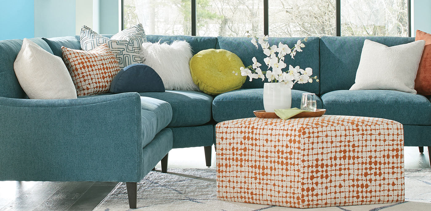 Contemporary blue sectional couch featuring vibrant orange and white throw pillows.