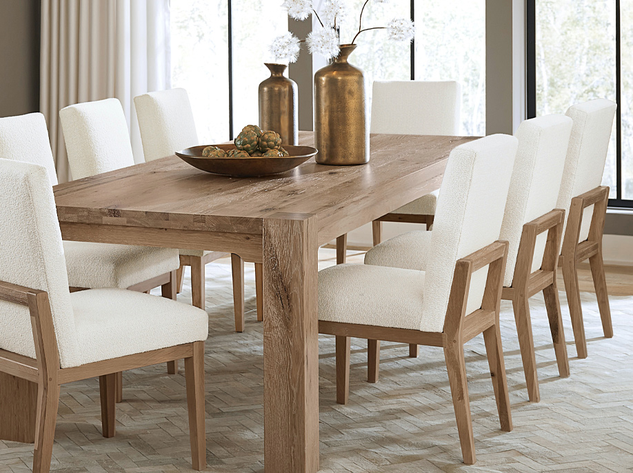 White chairs surrounding a wooden dining table in a bright room.